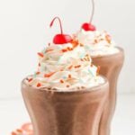 Two chocolate milkshakes with whipped cream and sprinkles.