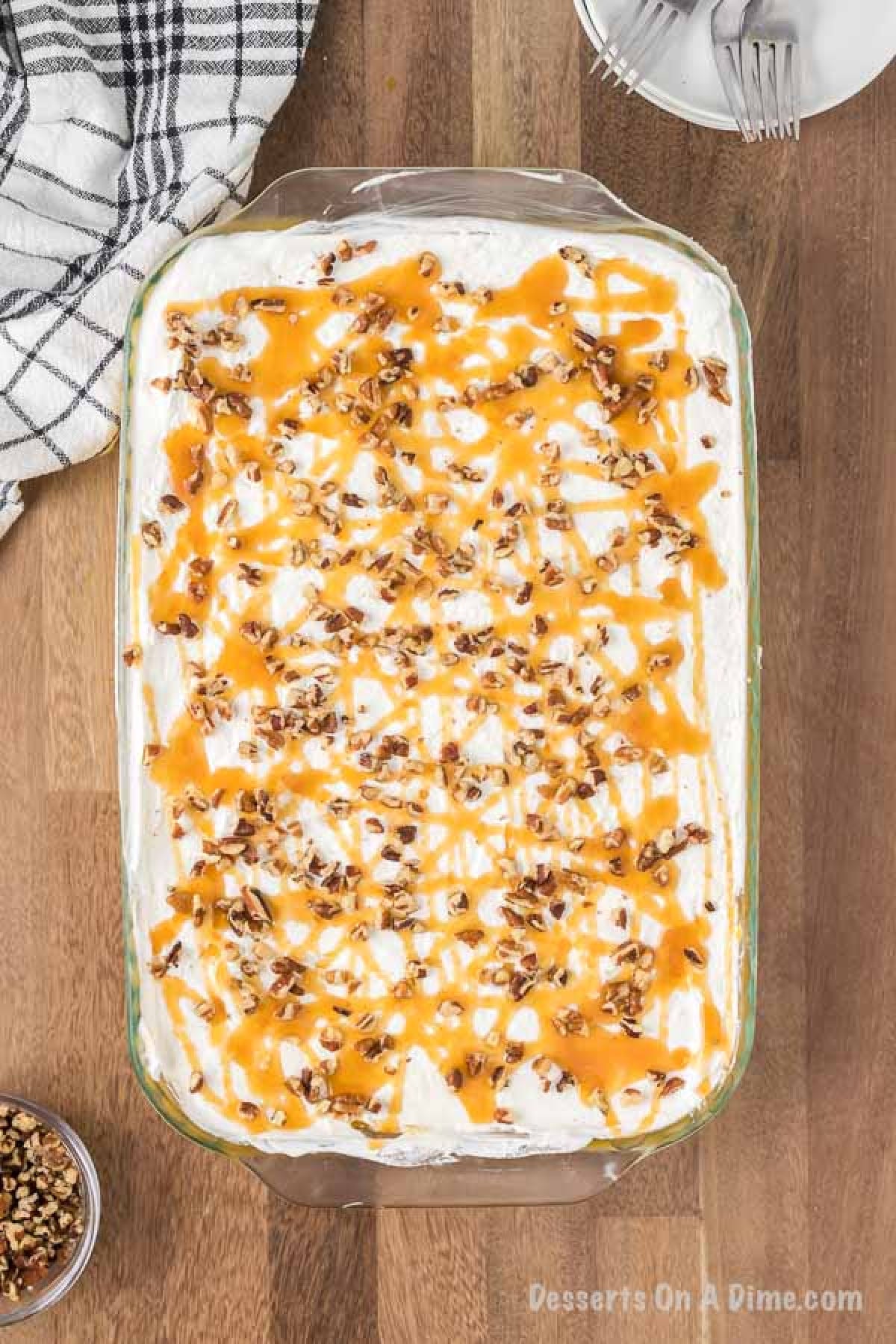 The finished lasagna in the baking pan topped with cool whip, drizzled with caramel on top and top with more chopped pecans.  