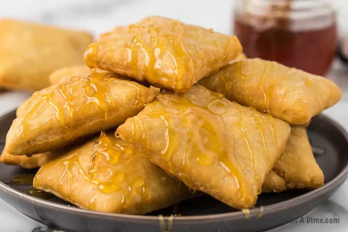Sopapilla Recipe piled on a plate and drizzled with honey.