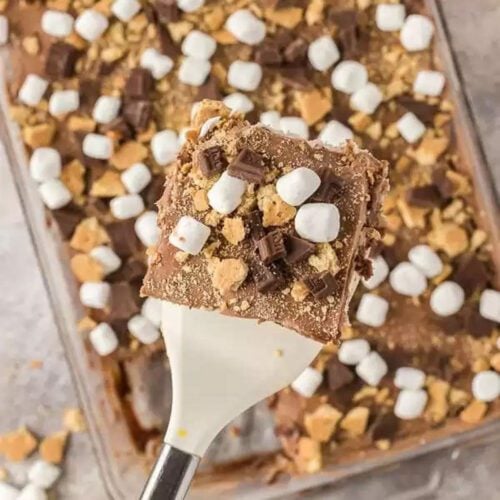 Smores poke cake topped with marshmallows, chocolate and graham crackers.