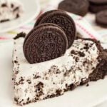 A piece of this no bake Oreo pie on a white plate with 2 Oreo Cookies in the top of the pie