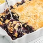 Blueberry cobbler in a white casserole dish with a spoon.