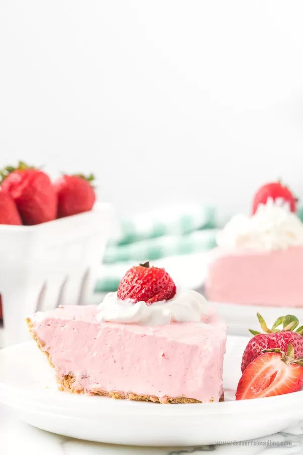 Strawberry jello pie recipe is an easy and classic dessert you can make in minutes. Retro Strawberry jello pie recipe is so light and fluffy and you only need 5 ingredients! Strawberry jello pie cool whip recipe with no bake graham cracker crust makes Strawberry jello pie easy. #dessertonadime #strawberryjellopierecipe Strawberry Jello pie with a side of slice strawberries on a white plate with a fork.