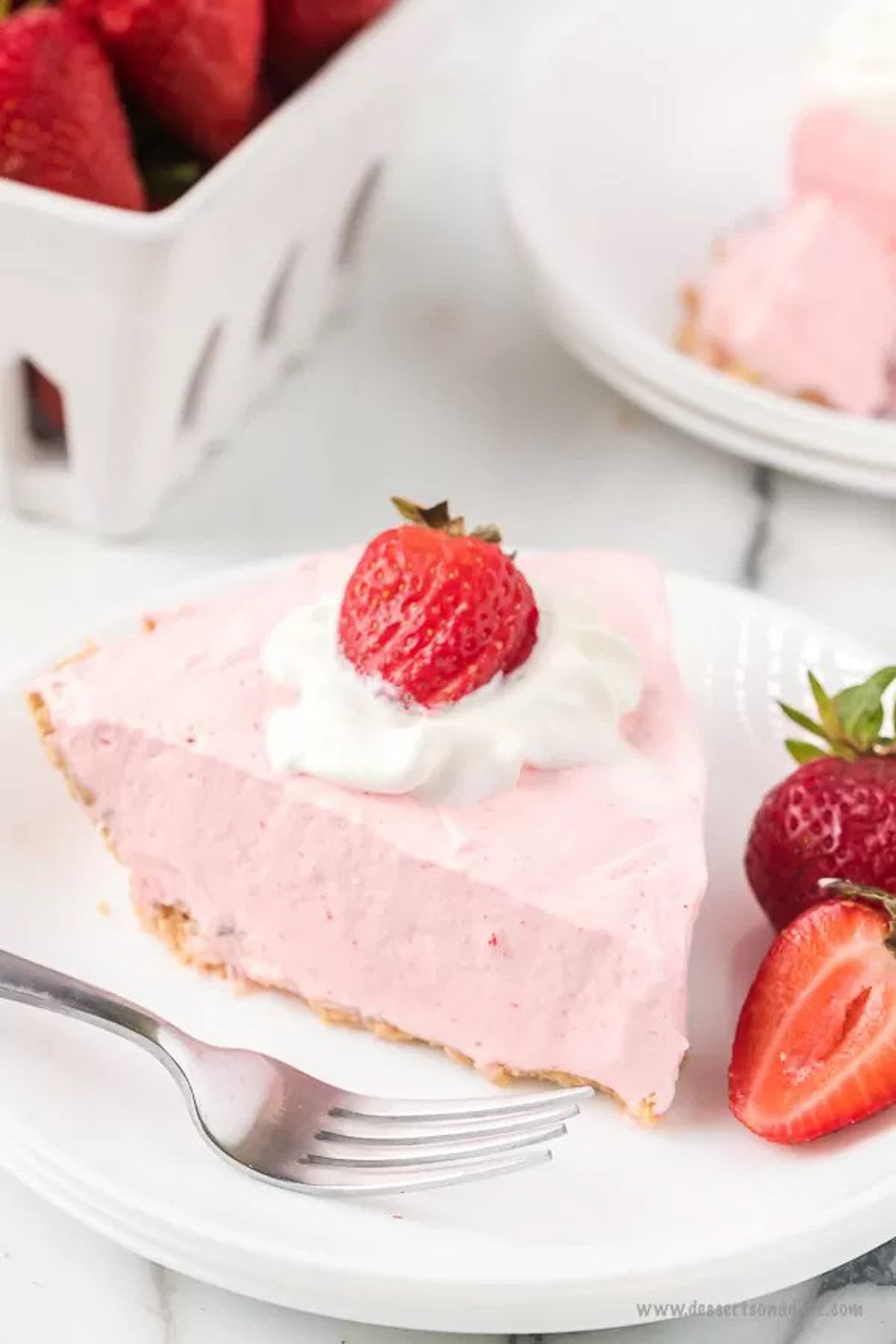 Strawberry jello pie recipe is an easy and classic dessert you can make in minutes. Retro Strawberry jello pie recipe is so light and fluffy and you only need 5 ingredients! Strawberry jello pie cool whip recipe with no bake graham cracker crust makes Strawberry jello pie easy. #dessertonadime #strawberryjellopierecipe Strawberry Jello pie with a side of slice strawberries on a white plate