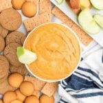 Pumpkin dip in a bowl surrounded with cookies and fruit on a tray.