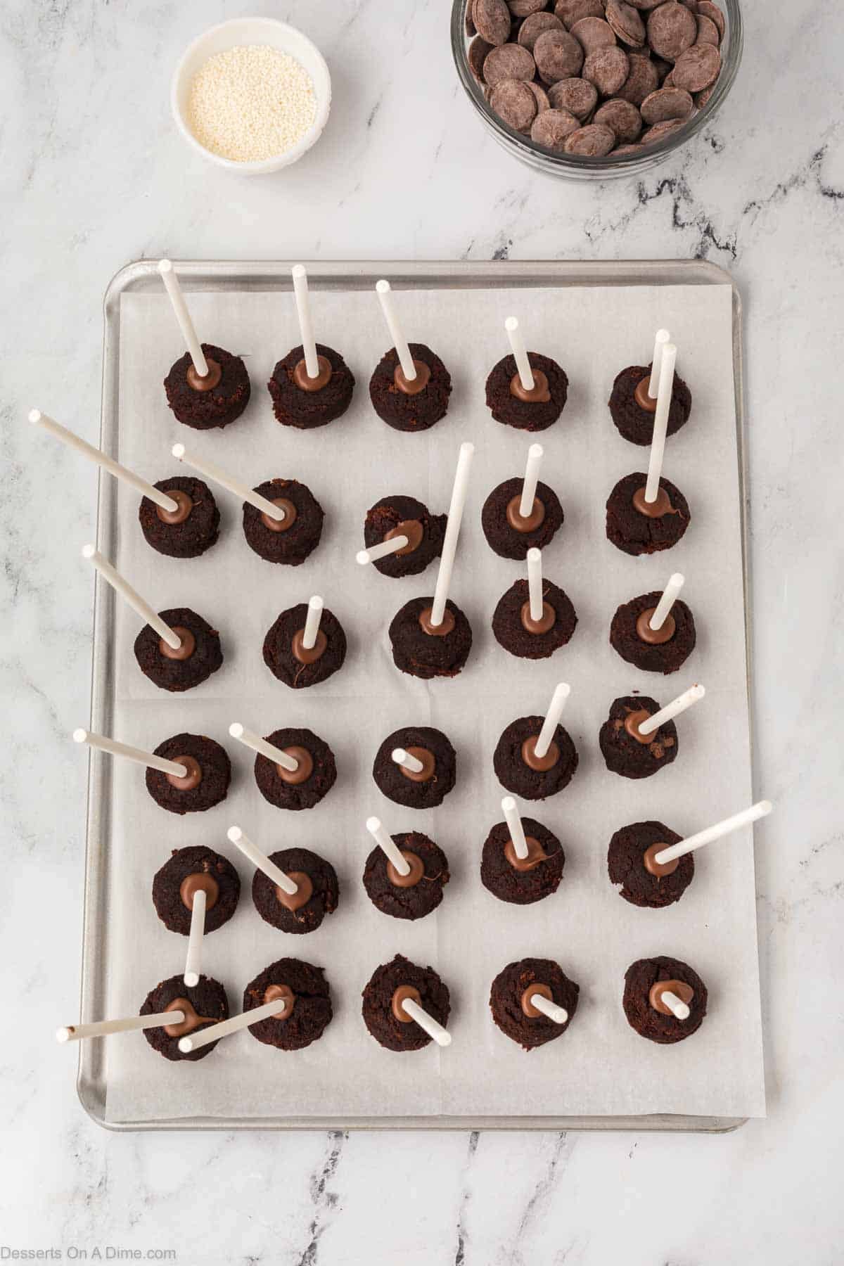 Cake pops with stick inserted on baking sheet.