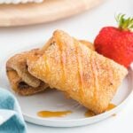 Chimichangas stacked on a white plate with caramel on top.