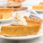 Pumpkin pie with whipped cream on a white plate.