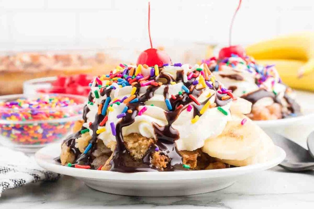 Banana Split Cake on a white plate topped with a cherry. 
