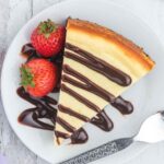 Brownie Batter Cheesecake with chocolate sauce on a white plate.
