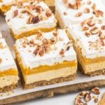 Creamy layered pumpkin dessert with whipped topping topped with chopped nuts and a graham cracker crust.