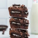 A stack of three oreo brownies with a glass of milk.