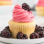 A cupcake with pink frosting and blackberries.