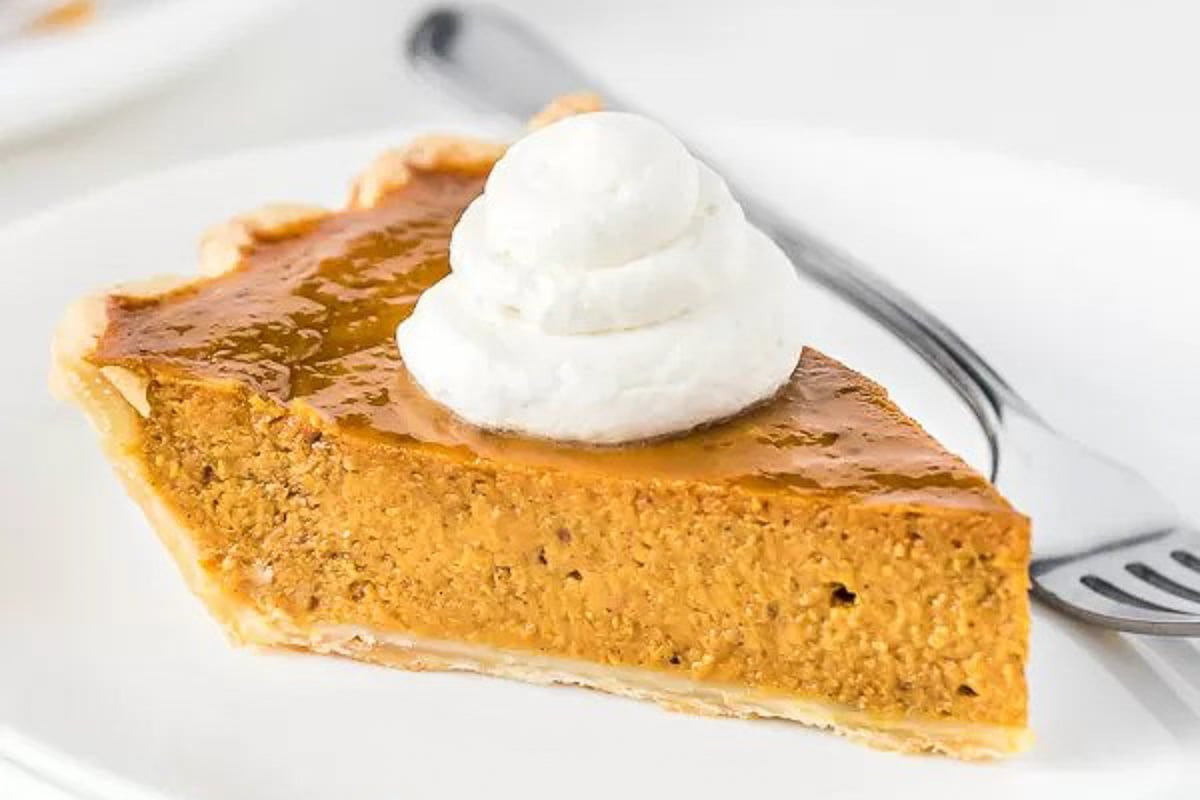 A slice of Pumpkin pie topped with whipped cream on a plate