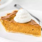 A slice of Pumpkin pie topped with whipped cream on a plate