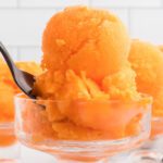 A spoon is holding a scoop of orange ice cream.