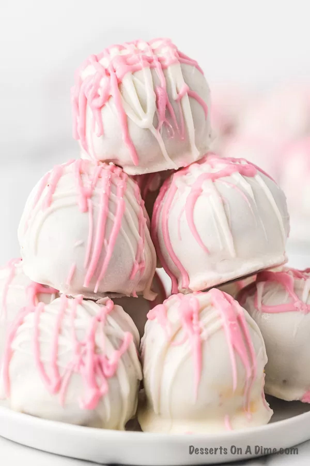 Red velvet cake balls with cream cheese dipped in white chocolate make an irresistible dessert. Bite size treats are so fun and this recipe for Red velvet cake balls does not disappoint. Try no bake red velvet truffles for Christmas, Valentines Day and more. Make this easy red velvet cake balls recipe for a delicious dessert. #dessertonadime #redvelvetcakeballs #Withcreamcheesewhitechocolate #EasyNoBake #redvelvetcakeballseasy #ChocolateCovered Red Velvet Cake Balls decorated and stacked on a platter