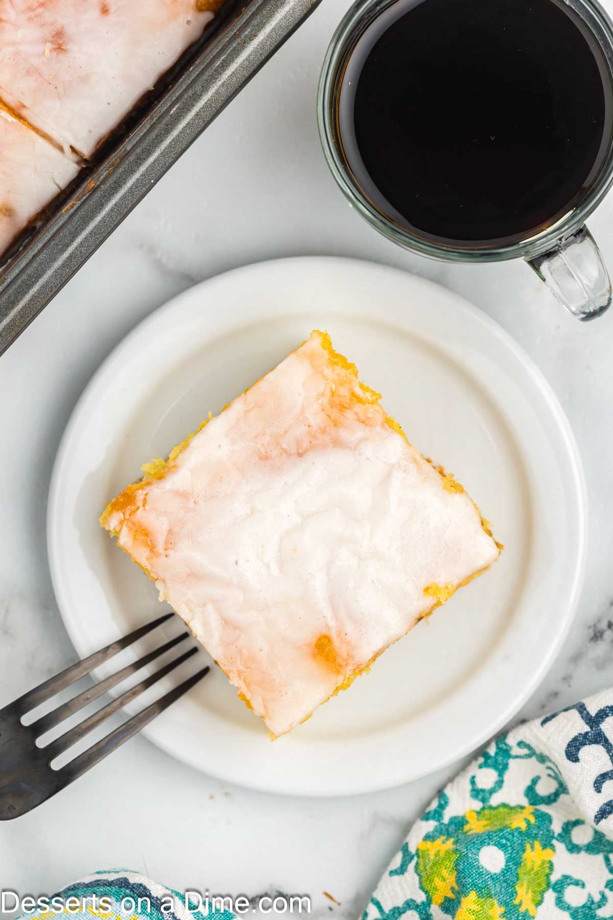 Slice of Honey Bun Cake on a plate beside a cup of coffee. 