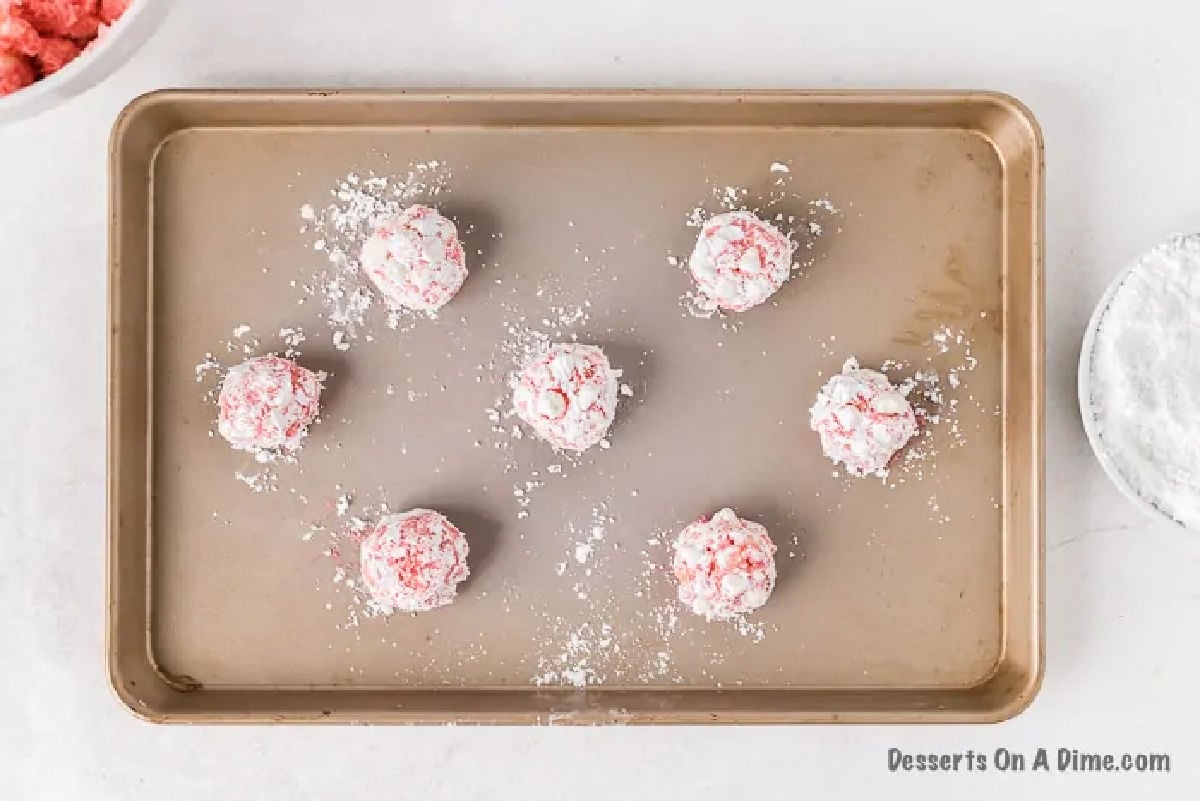 Dough balls with powdered sugar on baking sheet. 