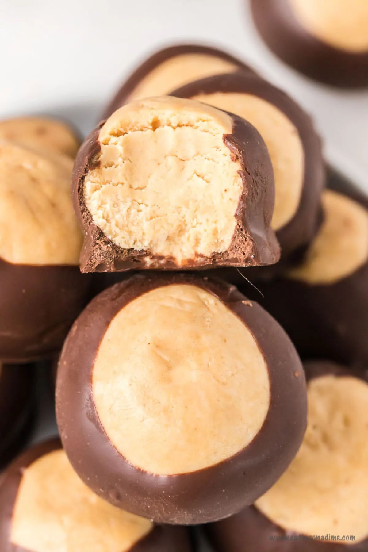 This no bake Buckeye balls recipe will be a hit for chocolate and peanut butter fans. Buckeye balls taste like peanut butter cups and melt in your mouth. This buckeye balls easy recipe is great for Christmas and no shortening required. #dessertonadime #buckeyeballsrecipe #buckeyeballsbest Buckeye Peanut Butter Balls stacked together. up close.