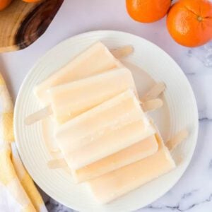 Orange popsicles on a white plate with oranges.