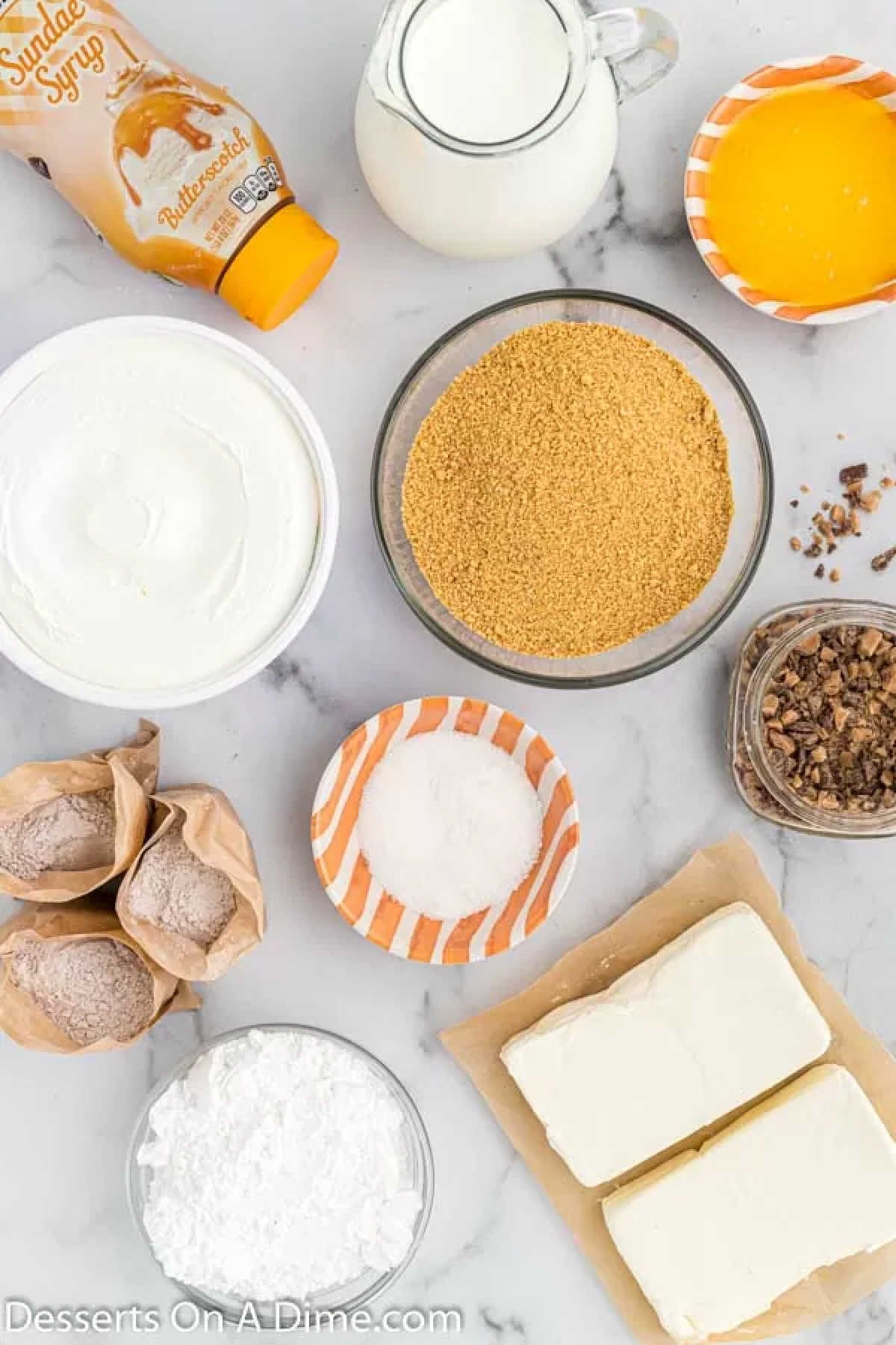 Ingredients for recipe - graham cracker crumbs, butter, cream cheese, whipped topping, pudding, milk, butterscotch sauce, heath bits.