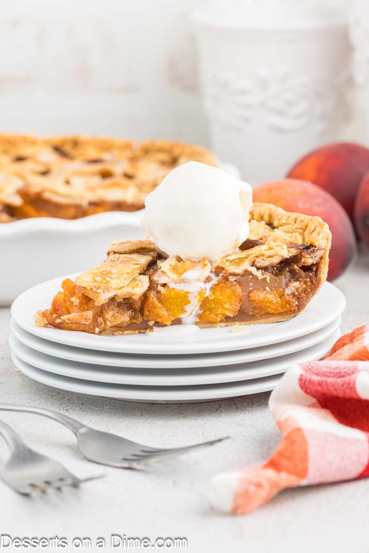 Slice of peach pie on white plate topped with ice cream. 