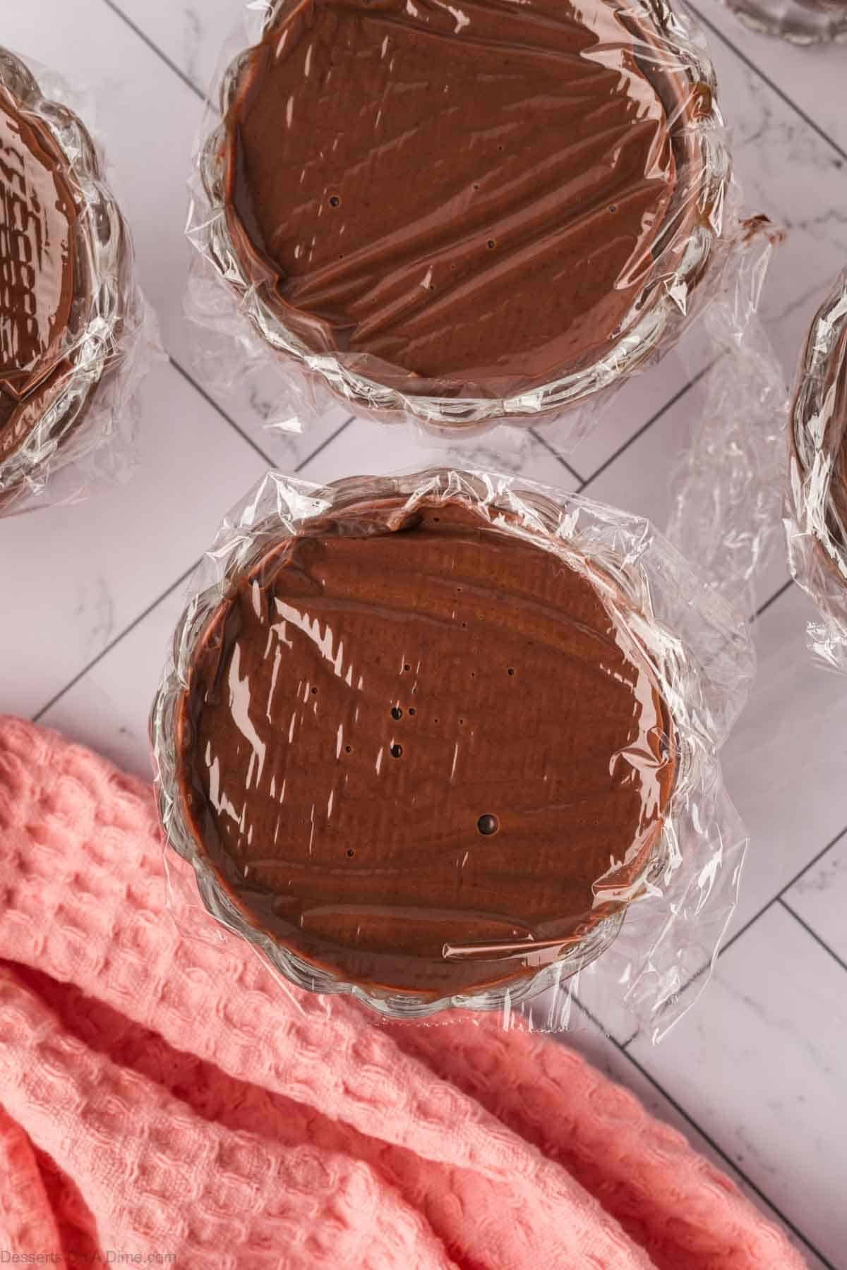Pudding mixture divided into cups and covered with plastic wrap.