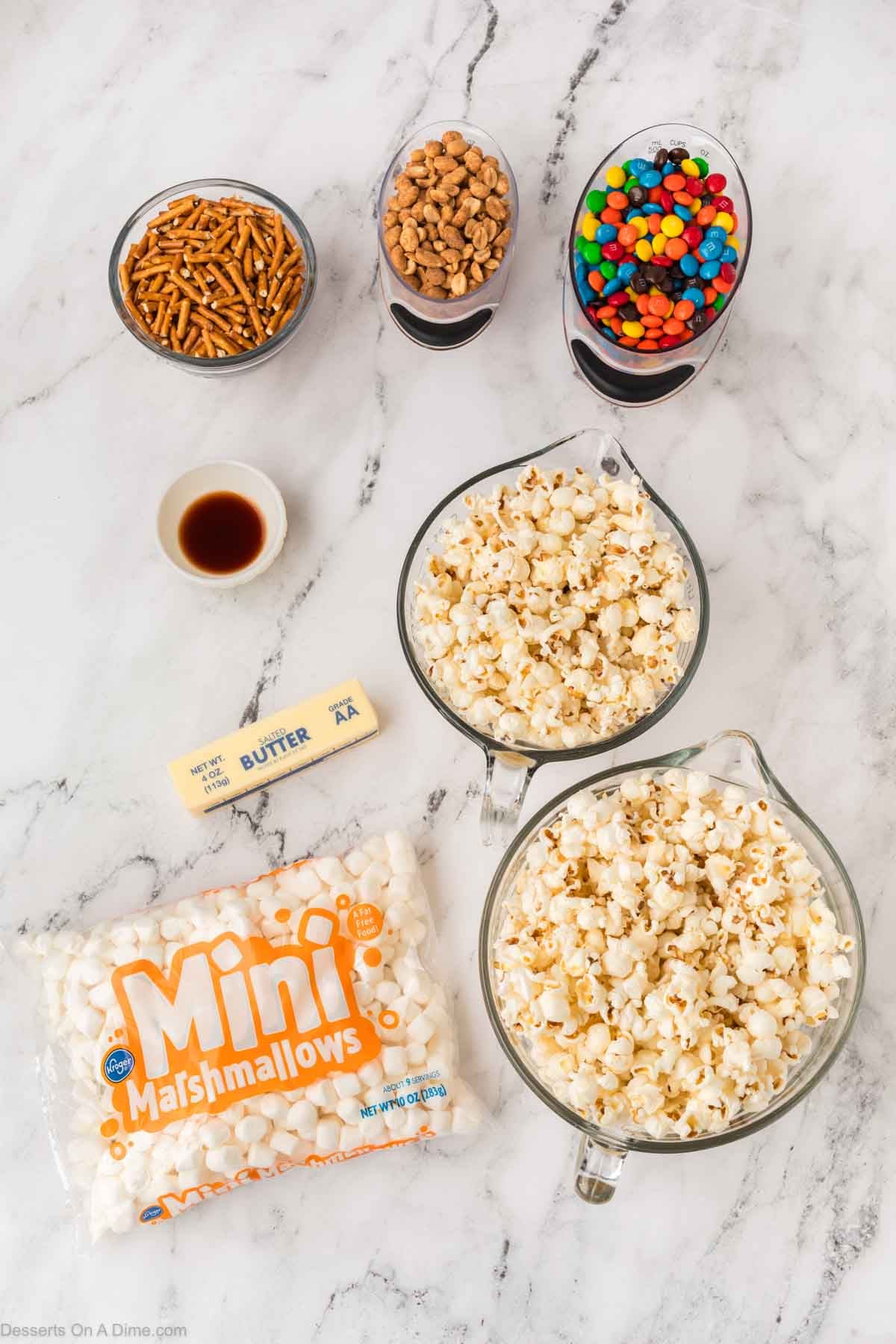 Ingredients for recipe - butter, marshmallows, vanilla, popcorn, m&ms, pretzel sticks. peanuts.