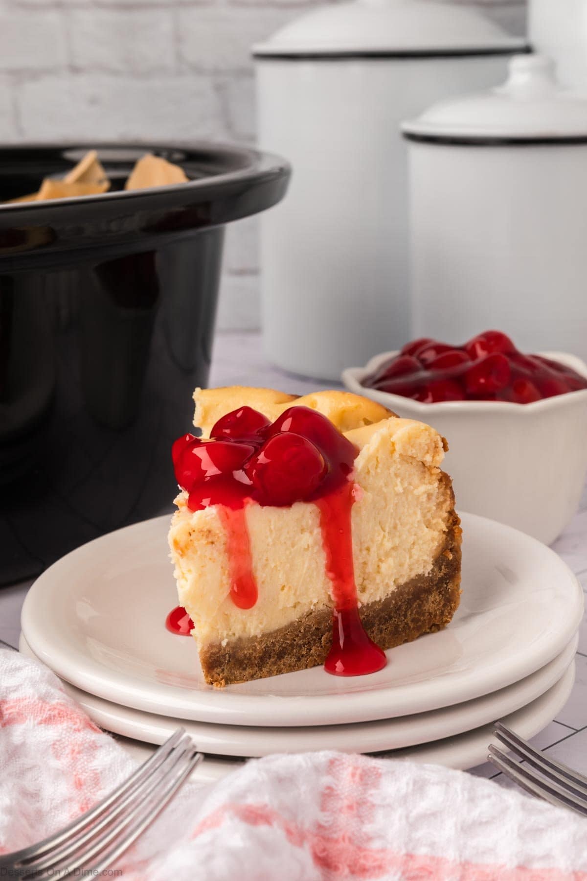 Slice of Cheesecake with cherry topping on a white plate. 