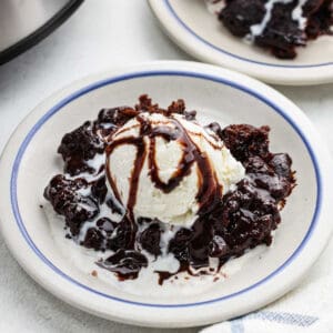 Crockpot brownies with ice cream and chocolate syrup in a white bowl.