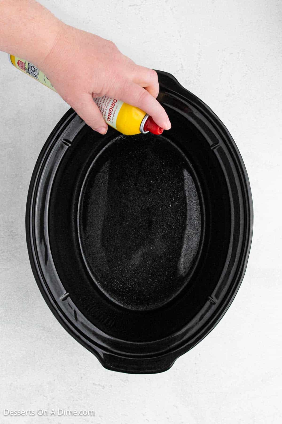 Crock pot being sprayed with cooking spray.