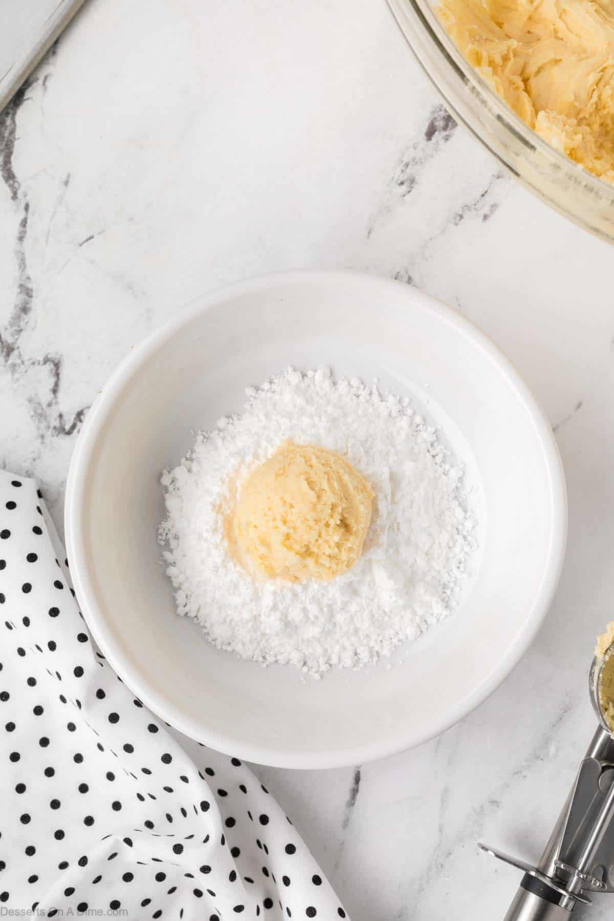 Dough balls dropped into powdered sugar in a bowl. 