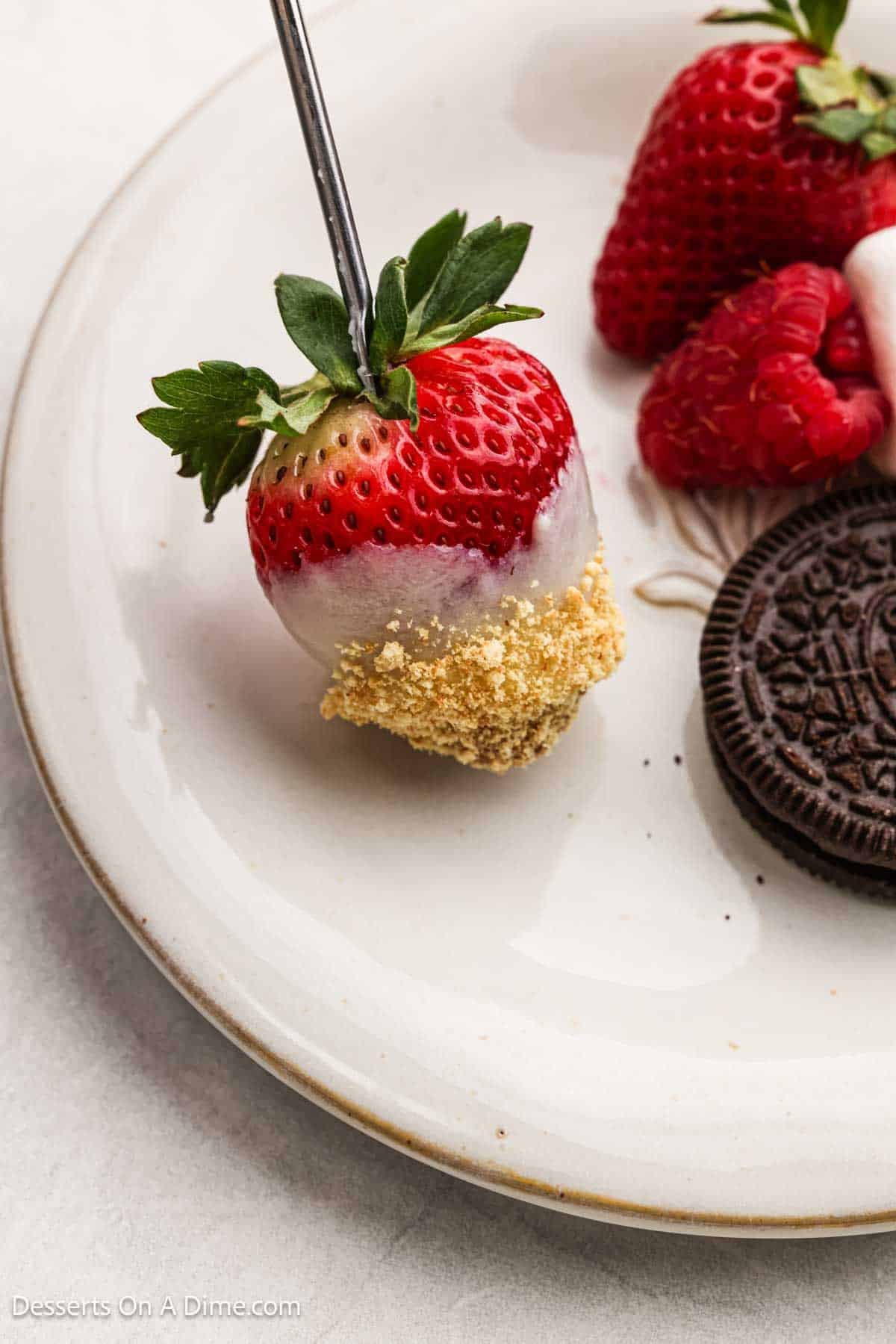 Strawberry coated in cheesecake fondue and served on a plate beside other dippers. 