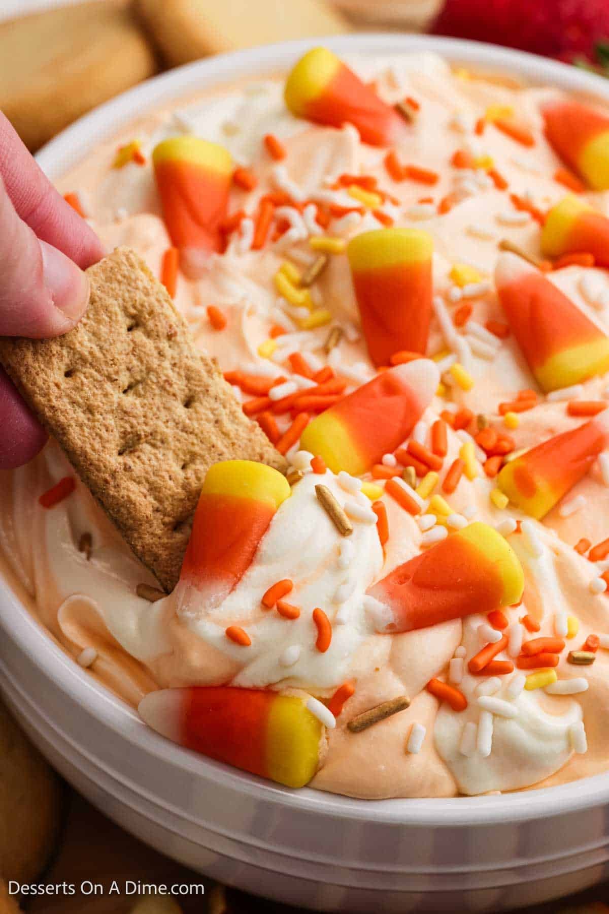 Orange dip in a bowl topped with sprinkles and candy.