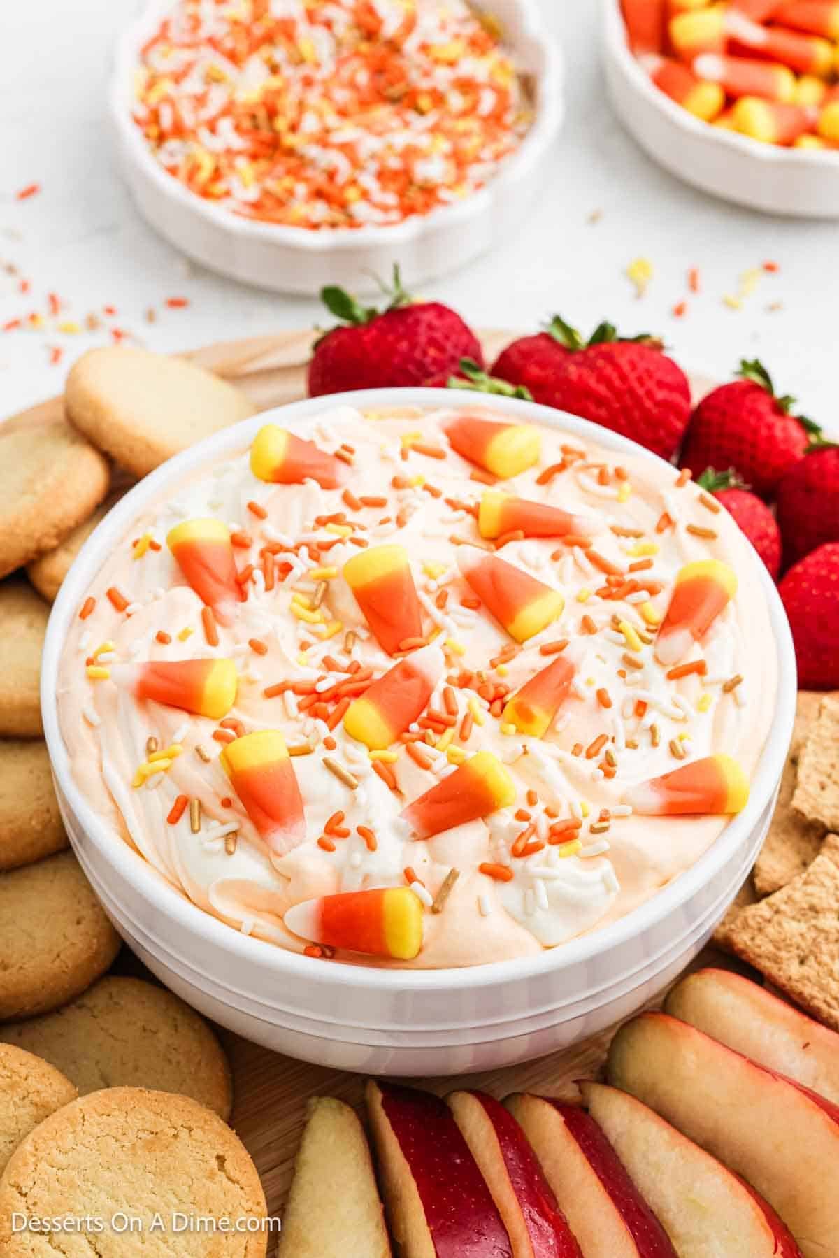 White serving bowl with dip mixture topped with sprinkles surrounded with fruit and cookies.