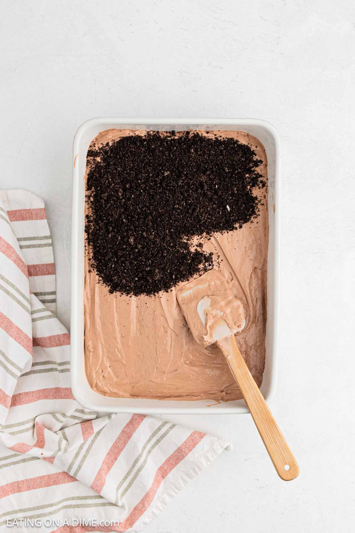 Crushed cookies being spread over pudding layer in baking dish.