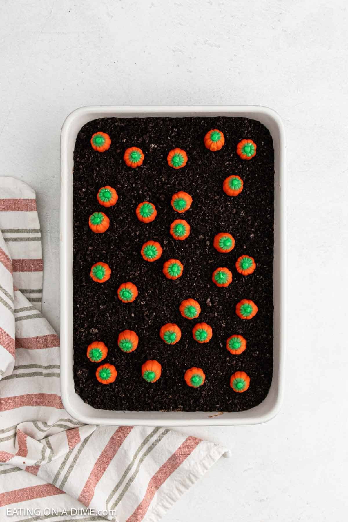 Mini candy pumpkins arranged on top of crushed cookies in baking dish. 