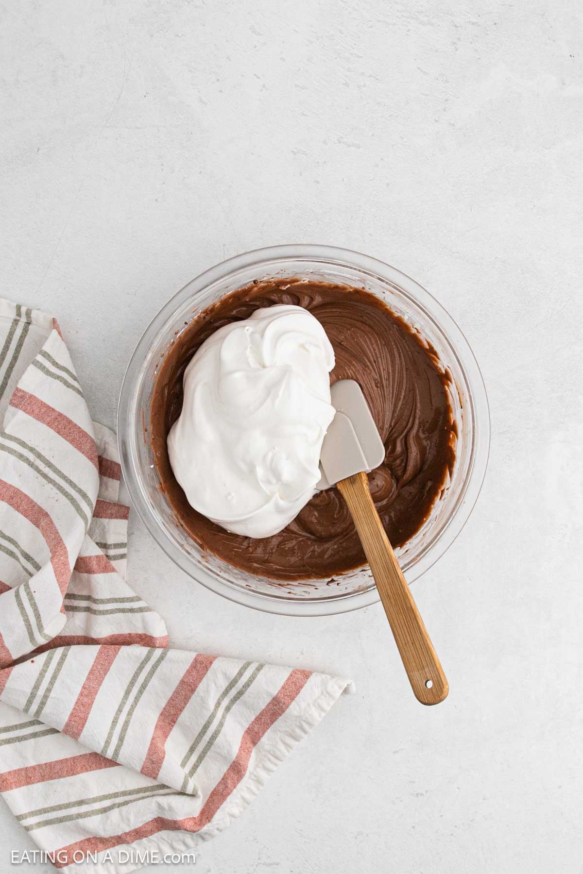 Whipped topping folded into pudding and cream cheese mixture in bowl.