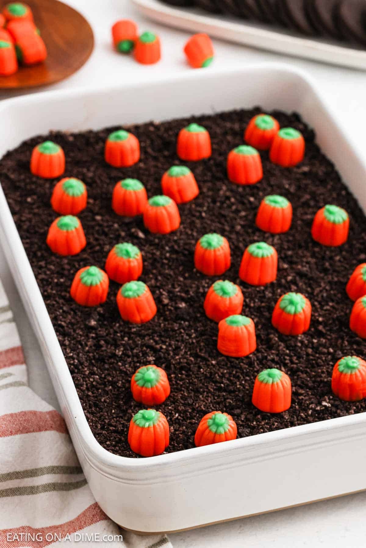 No bake dessert in a baking dish with crushed cookies and candy pumpkins on top. 